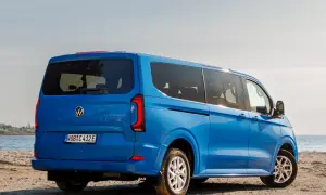 Błękitny VW Transporter T7 na piaszczystej plaży, z widokiem na morze.