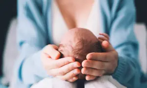 Delikatne dłonie otulają główkę noworodka, ukazując troskę i miłość. Szybko zarastające ciemiączko to naturalny proces, a ten obraz to dowód na to, jak szybko dzieci rosną.