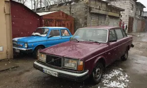 En vinröd Volvo 244 DLS står parkerad bredvid en blå bil i snöfall.