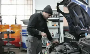 Mechanik sprawdza silnik, zastanawiając się, ile kosztuje roboczogodzina w warsztacie samochodowym.