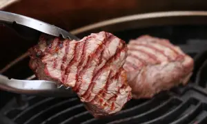 Zangen halten ein saftiges Stück Roastbeef über einem Grillrost. Das Fleisch hat schöne Grillstreifen und ist perfekt gegrillt.