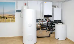 Nowoczesna kotłownia z dwoma kotłami gazowymi i zasobnikiem ciepłej wody. Obok wisząca szafka elektryczna i obraz z krajobrazem.