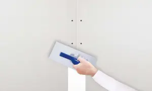 Ręka z kielnią nakłada gips szpachlowy na połączenie płyt gipsowo-kartonowych. Idealny do wygładzania i tworzenia równych powierzchni.