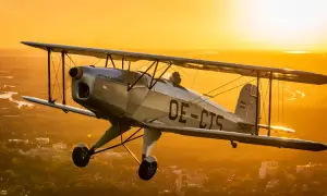 Ein silberner Doppeldecker fliegt im goldenen Abendlicht über einer Stadt. Ein Traum für alle, die gerne flugzeuge fotografieren.