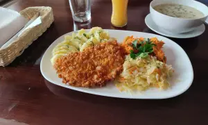 Talerz z panierowanym kotletem, ziemniakami, surówkami i zupą.