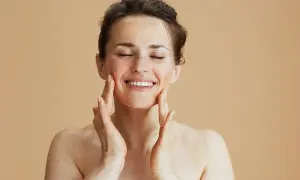 Kobieta z zamkniętymi oczami nakłada peeling na twarz, ciesząc się zabiegiem. Zastanawiasz się, jak często robić peeling twarzy?
