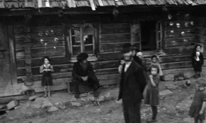 Kinder und Erwachsene stehen vor einem Holzhaus. Die Szene erinnert an die **Judenverfolgung** und die damit verbundene Not.