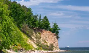 Plaża z klifem i lasem, idealne atrakcje nad morzem. Ludzie spacerują, odpoczywają, a na horyzoncie widać statek.