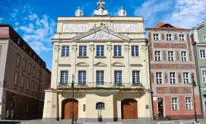 Pałac Działyńskich w Poznaniu, z bogatymi zdobieniami i orłem na szczycie, dumnie prezentuje się na tle błękitnego nieba.
