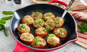 Pomodori gratinati in padella, ripieni di pangrattato e erbe aromatiche, guarniti con basilico fresco.