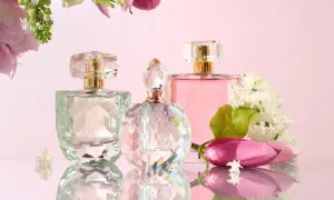 Trzy flakoniki perfum i kwiaty na różowym tle.