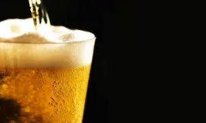 Birra ghiacciata che cola in un bicchiere, creando una schiuma densa e invitante. Le bollicine danzano nel liquido dorato.