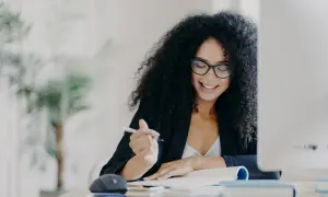 Mujer sonríe mientras escribe, pensando en como empezar una carta de motivación.