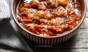 Seppie in padella, succulente e profumate, servite in una ciotola marrone con un contorno di tovagliolo grigio.