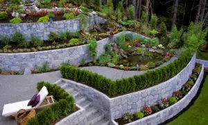 Giardino terrazzato con laghetto e cascata. Muri in pietra che creano livelli, illustrando la differenza tra muro di sostegno e muro di contenimento.