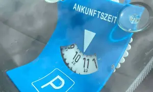 Blaue Parkscheibe mit der Aufschrift "ANKUNFTSZEIT". Die Scheibe ist auf 10:30 Uhr eingestellt, was 15 Minuten Parkzeit bedeutet.