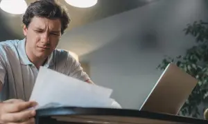 Mężczyzna zamyślony nad dokumentami, być może analizuje fakturę na osobę fizyczną. Obok laptop.