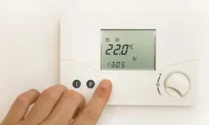 Dłoń naciska przycisk na termostacie pokazującym 22°C.