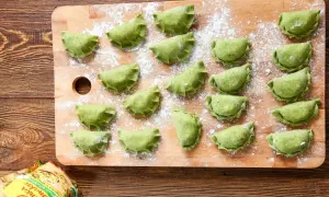 Zielone pierogi ze szpinakiem i serem feta ułożone na desce, posypane mąką.