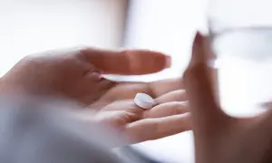 Dłoń trzyma tabletkę, zastanawiając się, czy tabletka "dzień po" to grzech. Obok szklanka wody.