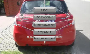 Czerwony Suzuki Swift z etykietami informującymi o światłach: STOP, POZYCYJNE, KIERUNKOWSKAZY, COFANIA, PRZECIWMGŁOWE.