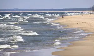 Plaża nad wzburzonym morzem, dwie osoby spacerują brzegiem.
