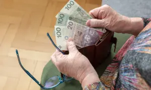 Dłoń starszej osoby wyjmuje z portfela polskie banknoty. Może to symbolizować dodatek do emerytury po 75 roku życia.