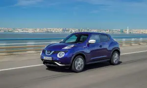 En blå Nissan Juke kör på en bro med en stad i bakgrunden. En perfekt bild för ett nissan juke test.