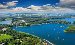 Malownicze jeziora i lasy Warmia i Mazury, idealne na wakacyjne atrakcje. Żaglówki pływają po błękitnej wodzie, a zielone wyspy kuszą spokojem.