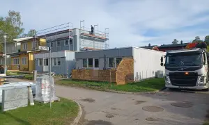 Byggnadsarbetare på ställningar vid hus som ska bygga till. En kranbil står parkerad.
