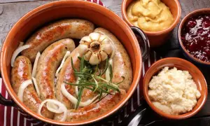 Pyszna kiełbasa z piekarnika w glinianym naczyniu, z cebulą, czosnkiem i rozmarynem. Obok musztarda, żurawina i chrzan.