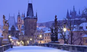 Praga zimą. Śnieg pokrywa Most Karola, wieże i dachy. W oddali widać zarys zamku.