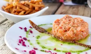 Tatar z łososia do sushi, podany z sosem i posypką z sezamu, obok miseczki frytek.