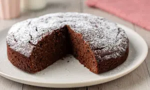 Una fetta è stata tolta da questa torta al cioccolato soffice, cosparsa di zucchero a velo.