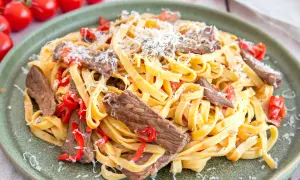 Pasta mit Rinderfiletstreifen, garniert mit geriebenem Parmesan und roten Paprikastücken. Ein köstliches Gericht, das zum Genießen einlädt.