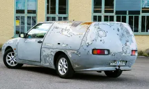 En sliten Saab 600, med rostfläckar och avskavd lack, står parkerad framför en gul byggnad med gröna fönster.