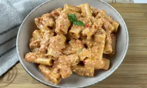Rigatoni conditi con un cremoso pesto di pomodorini e ricotta, guarniti con basilico fresco.