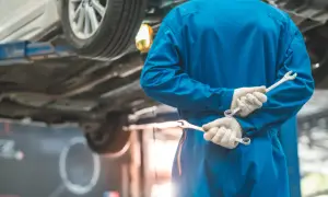 Meccanico in tuta blu con chiavi inglesi, pronto per i tagliandi auto. L'auto è sollevata sul ponte.