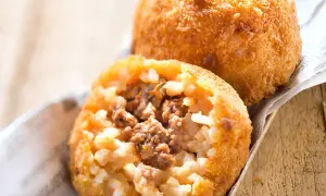 Deux arancini bolognaise dorés et croustillants, l'un ouvert révélant un cœur de riz et de viande savoureux.