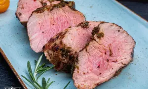 Saftiges Schweinefilet, perfekt gegrillt. Die Kerntemperatur ist entscheidend für dieses zarte Ergebnis. Rosmarin und Tomaten garnieren den Teller.