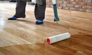 En person applicerar hårdvaxolja på ett trägolv med en roller. Golvet får en varm, skyddande yta.