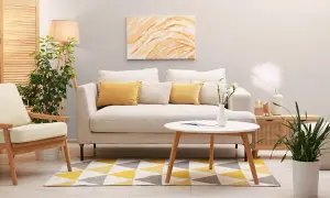 Jasny salon z sofą w kolorze platyny, żółtymi poduszkami i geometrycznym dywanem.