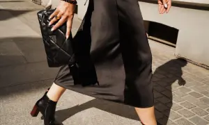 Eleganckie, czarne botki na obcasie idealnie pasują do zimowej sukienki. Kobieta trzyma pikowaną kopertówkę.