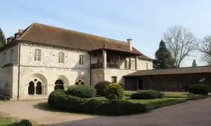 Bâtiment en pierre avec des arches romanes, un balcon et un jardin.