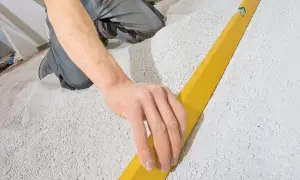Hand gleicht Schüttung für trockenestrich verlegen mit Richtlatte aus.