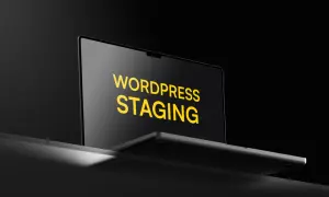 Laptop z napisem "WORDPRESS STAGING" na ekranie, w ciemnym otoczeniu.