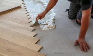 Un operaio stende la colla per posare un nuovo pavimento in legno. Scopri quanto costa rifare il pavimento.