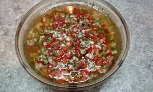 Un tazón de salsa criolla, con trozos picados de tomate, cebolla y pimiento rojo, flotando en un líquido claro.