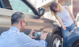 Man fotograferar parkeringsskada. Kvinnan undersöker skadan, en parkeringsskada smitning.