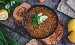 Herzhafte italienische Linsensuppe mit Karotten und Sellerie, garniert mit Zitrone und Petersilie, daneben Brot und frische Kräuter.